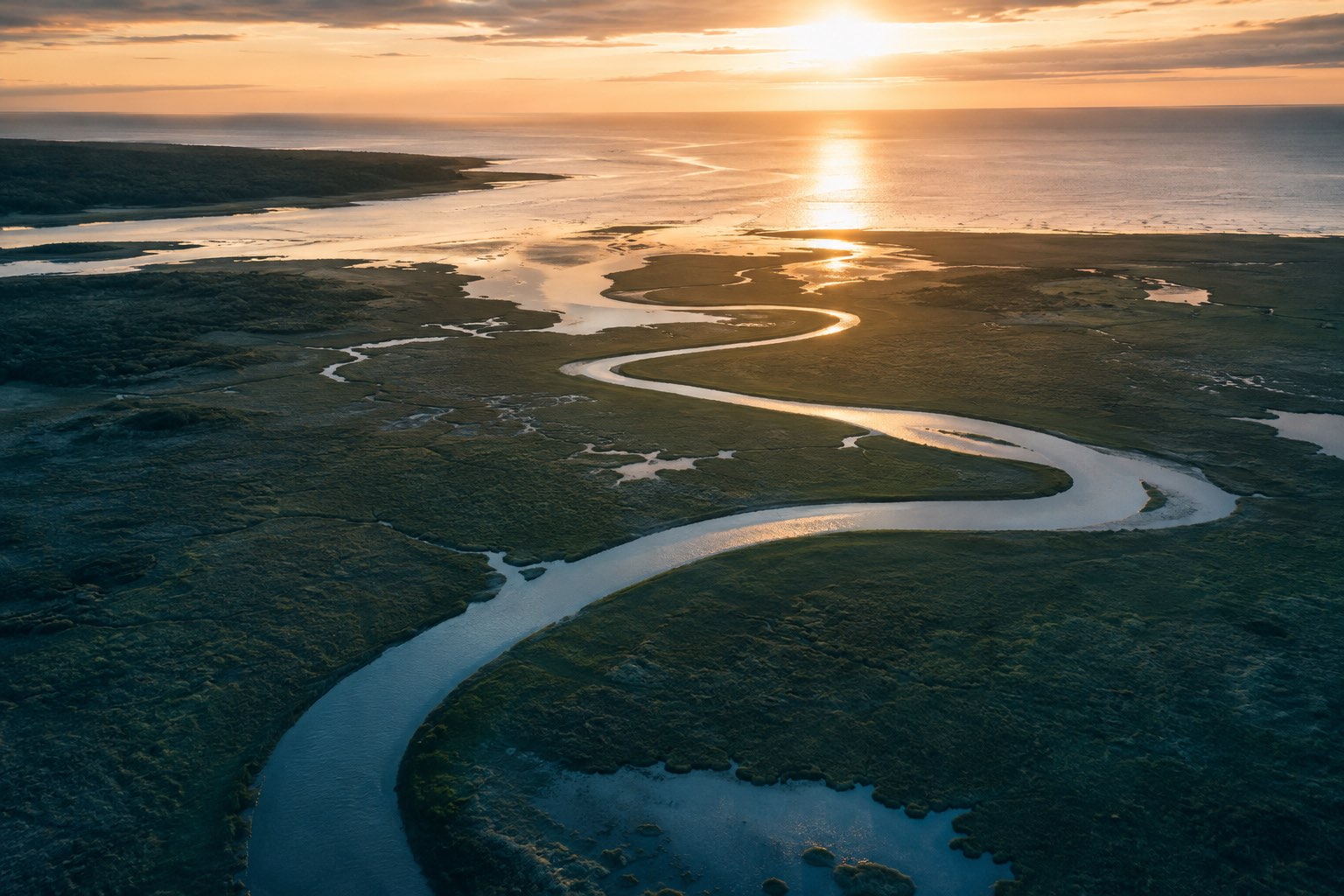 Aerial view of a tidal river winding through salt marsh toward the Atlantic at sunset.